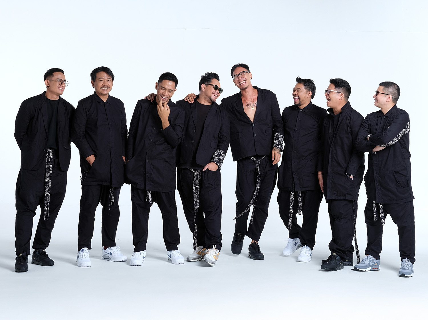 The eight members of SATS in black suits against a white backdrop